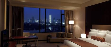 A hotel room with a large window, a bed, a desk, and a chair.