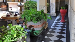 A hotel corridor with checkered flooring, potted plants, and a reception area with a counter and chairs. - Hotel Bahia Blanca (Santa Marta)