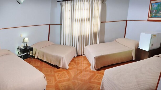 A hotel room with two single beds, a nightstand with a lamp, a window with curtains, and a painting on the wall. - Hotel Bahia Blanca (Santa Marta)