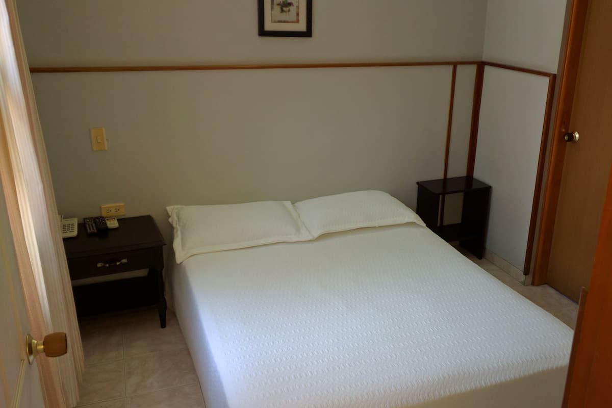 Een slaapkamer met een bed, nachtkastje en deur.