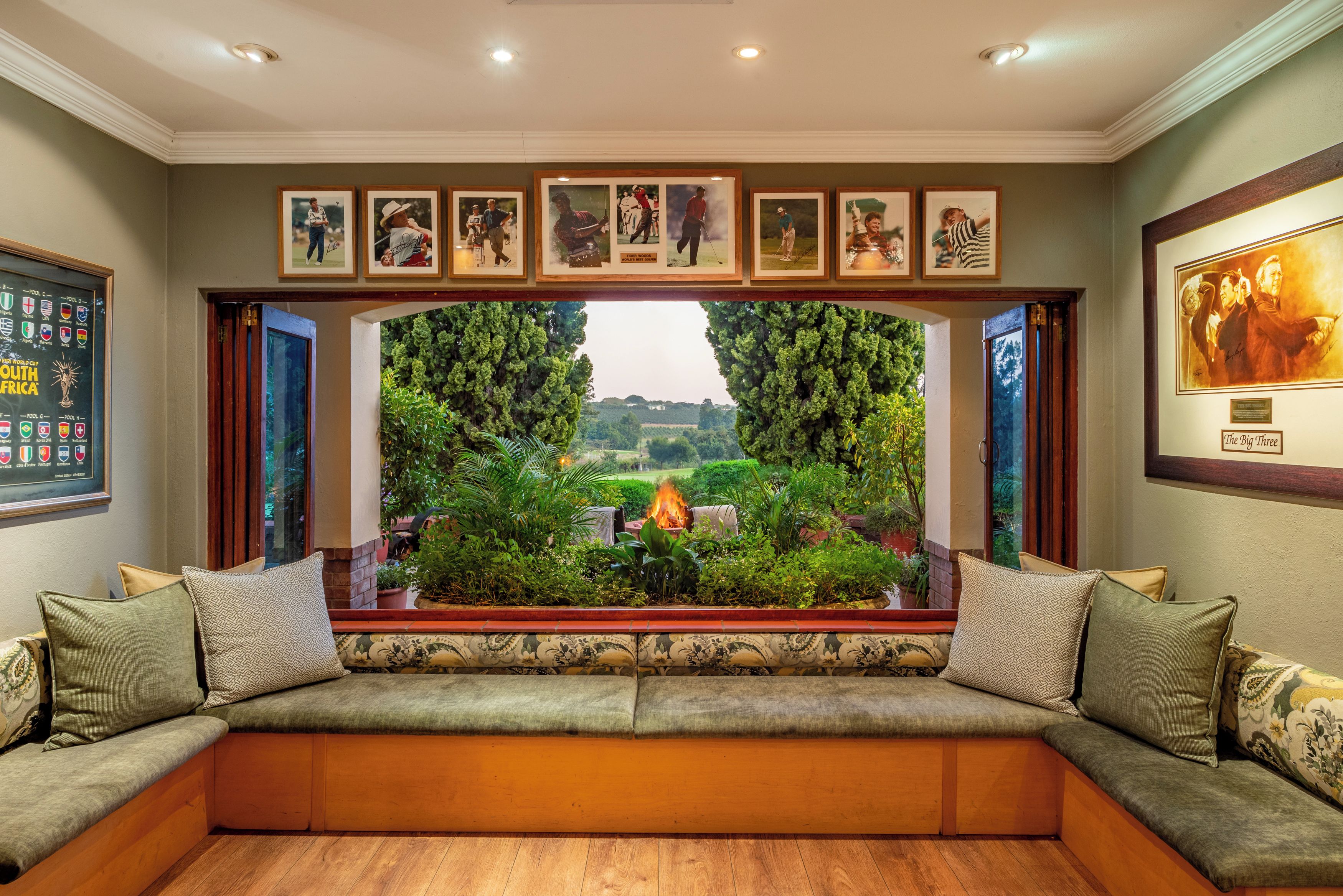 A room with a built-in bench seating area, framed sports memorabilia on the wall, and a view of a landscaped garden.