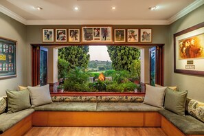 A room with a built-in bench seating area, framed sports memorabilia on the wall, and a view of a landscaped garden. - Oliver's Restaurant & Lodge (Mbombela)