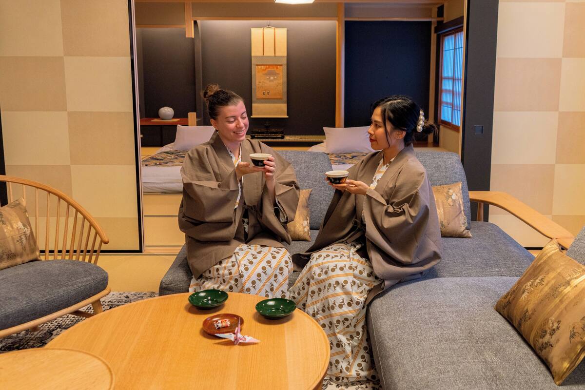 A room with a sofa, a round wooden table, and a bed with a headboard.