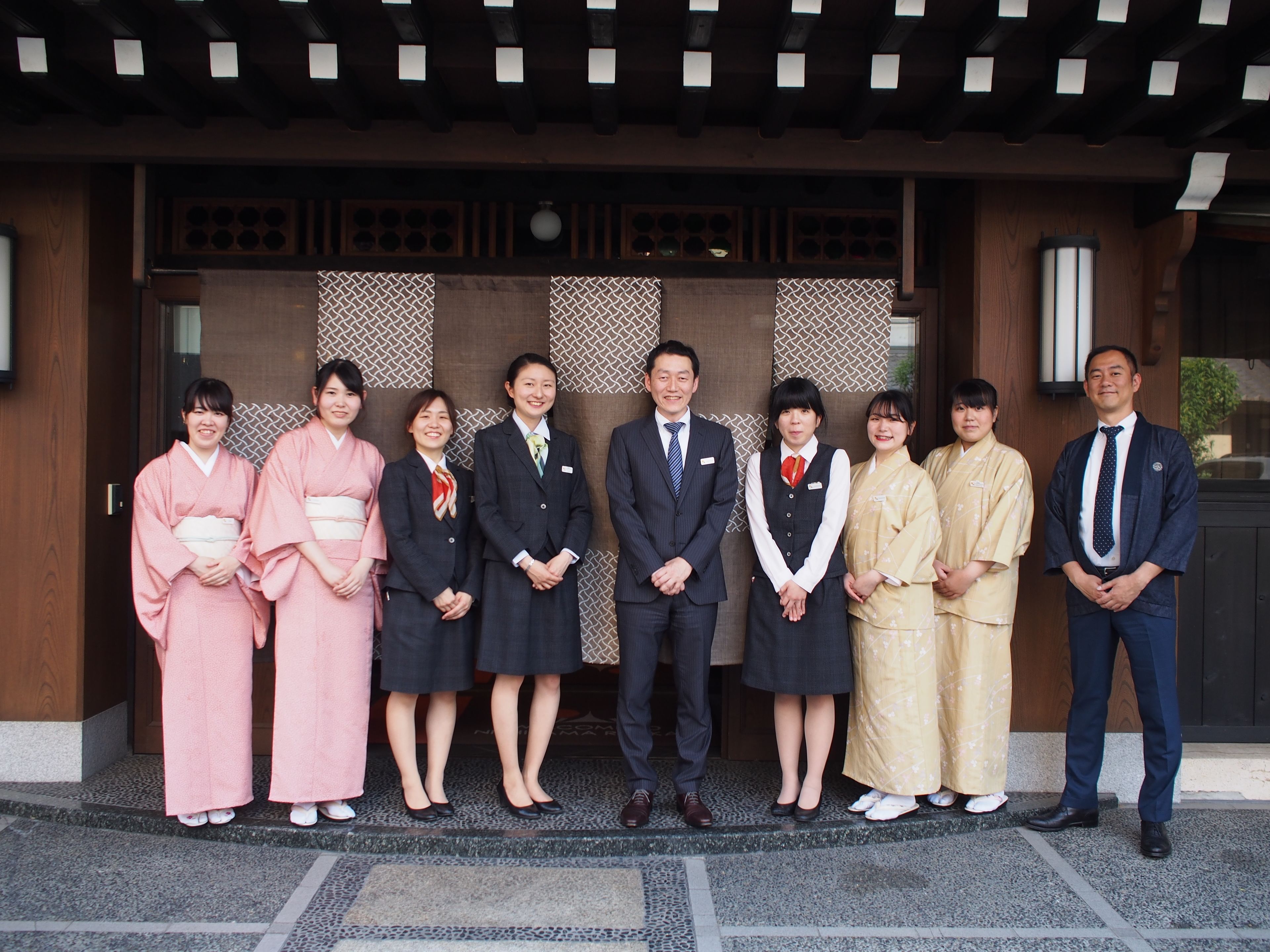 A group of people standing in front of a traditional building with a wooden facade and patterned wall decorations.
