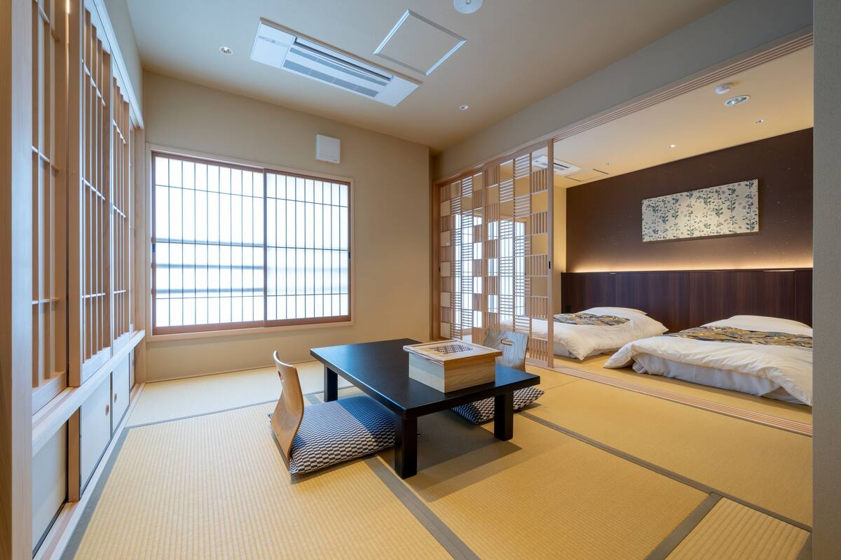 A traditional Japanese room with tatami flooring, a low table, two beds, and sliding doors.
