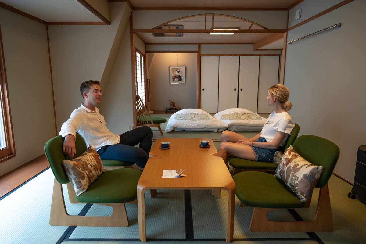 A room with a low wooden table, green chairs, and a traditional Japanese-style bed with pillows.