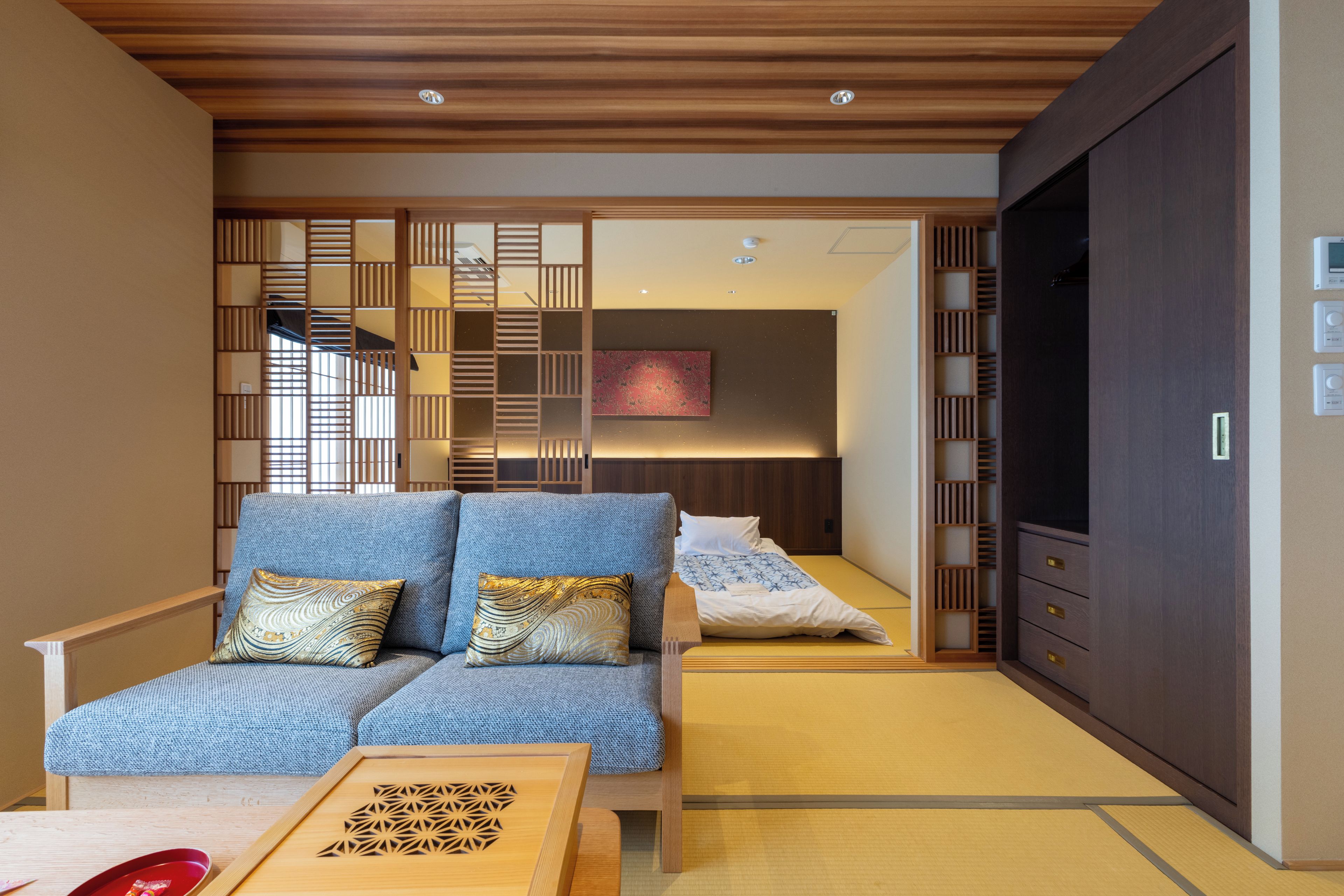 A modern interior with a sofa, a wooden table, and a sliding door leading to a bedroom.