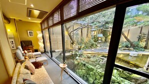 Ein modernes Wohnzimmer mit einem großen Fenster mit Blick auf einen Garten. Ein Sofa mit Kissen und ein kleiner Tisch mit einer Pflanze sind zu sehen.