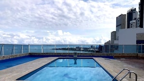 Piscina en la azotea con vistas despejadas de un horizonte urbano y una masa de agua al fondo.