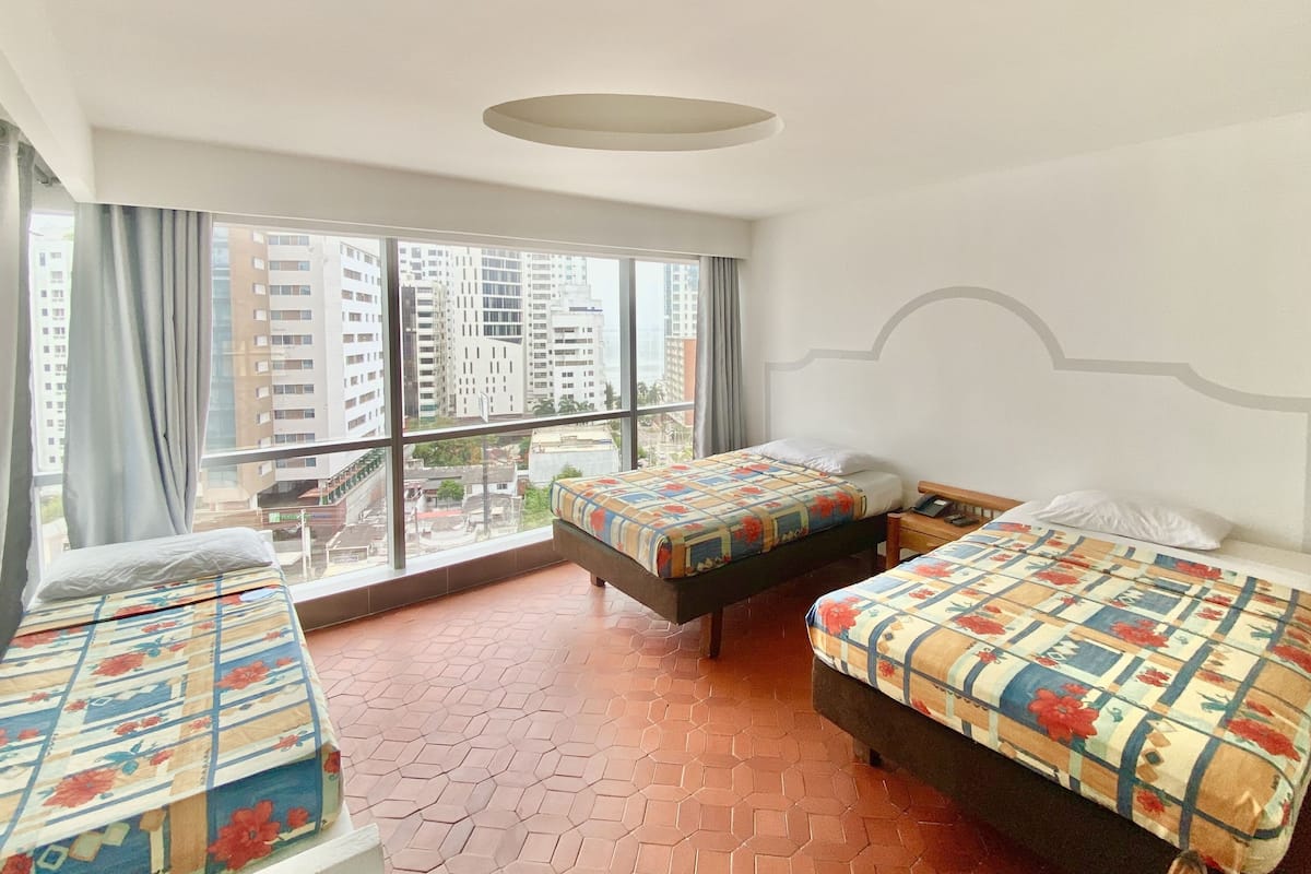 A hotel room with two beds, large windows, and a view of buildings.