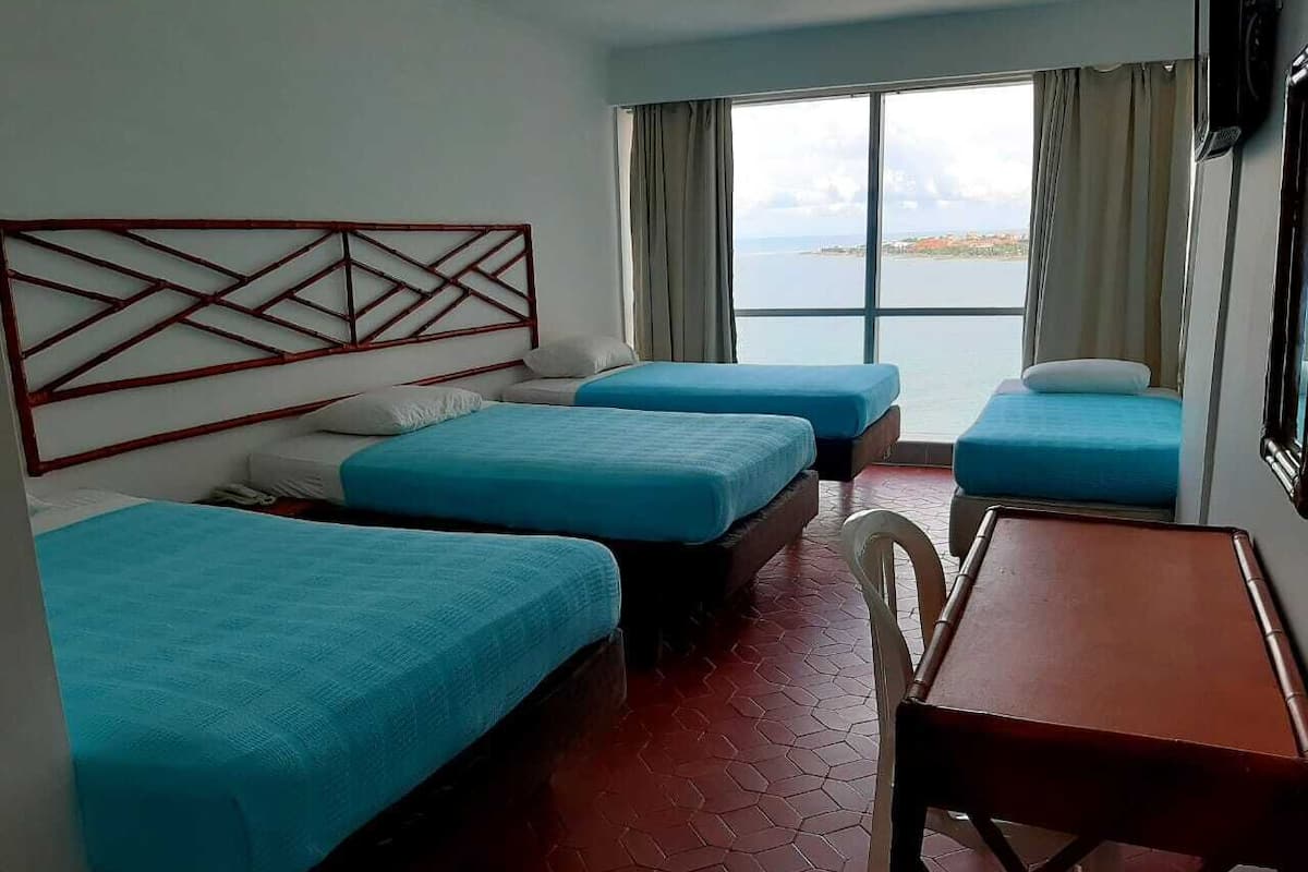 A hotel room with three beds, a wooden table, and a view of the sea.
