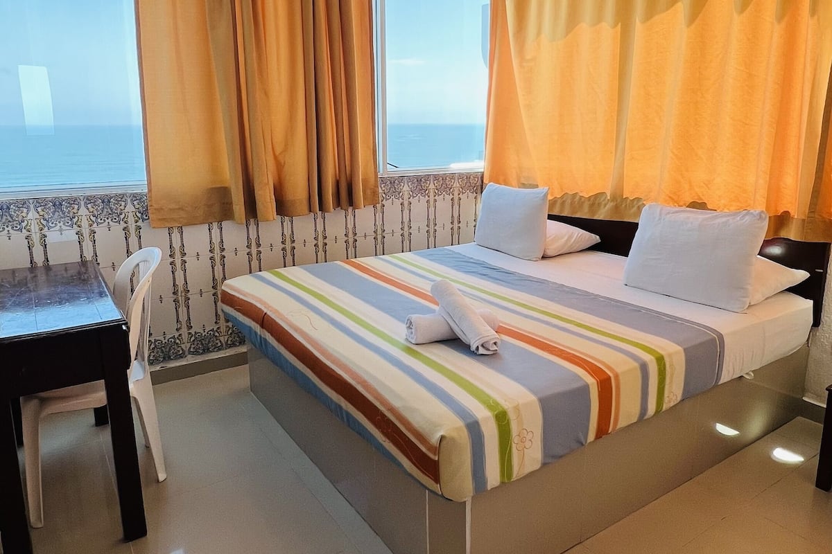 A hotel room with a large bed, a desk, and a view of the sea.