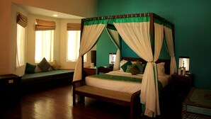 Una cama con dosel, un banco y un sofá en una habitación con paredes color turquesa y suelo de madera.