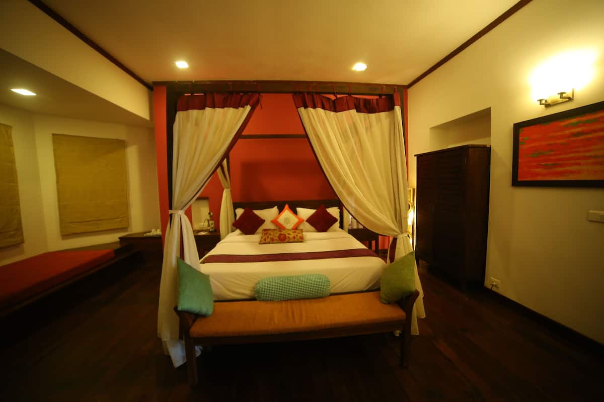 Habitación de hotel con cama, cortinas, un banco y un cuadro en la pared.