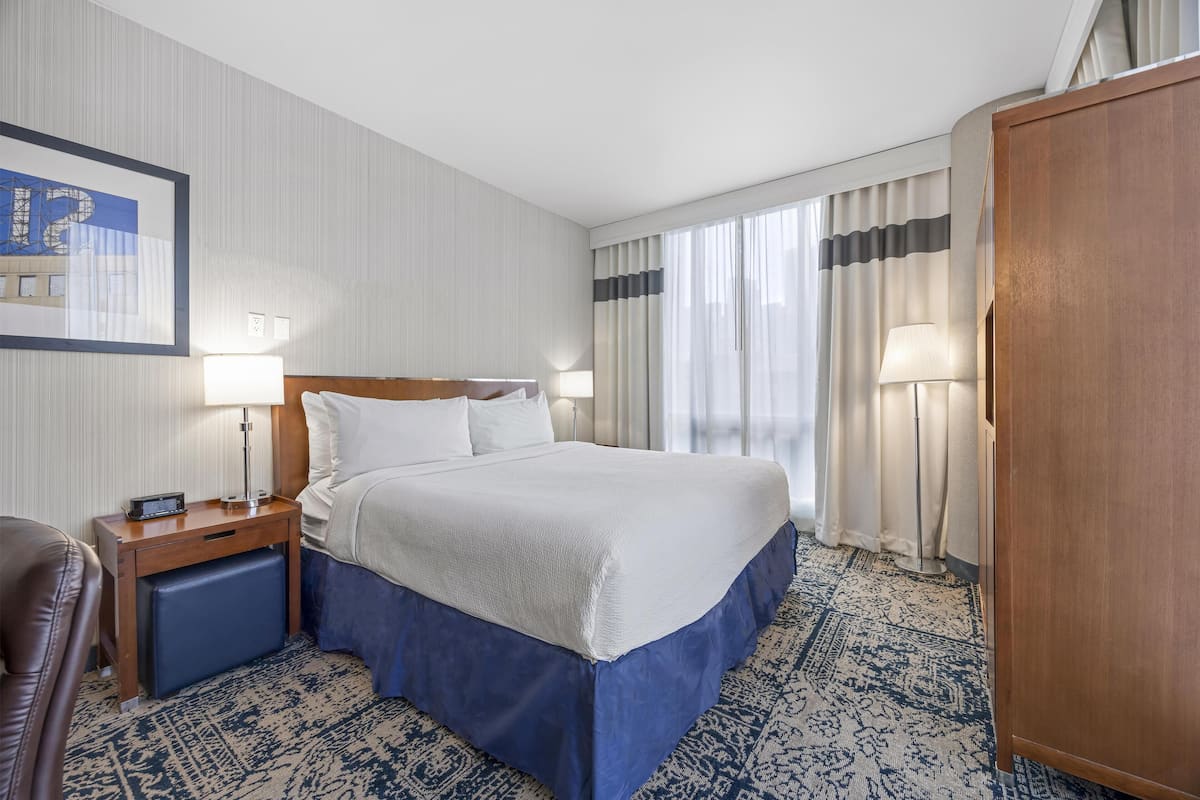A hotel room with a large bed, two bedside tables with lamps, a wooden wardrobe, and a patterned carpet.