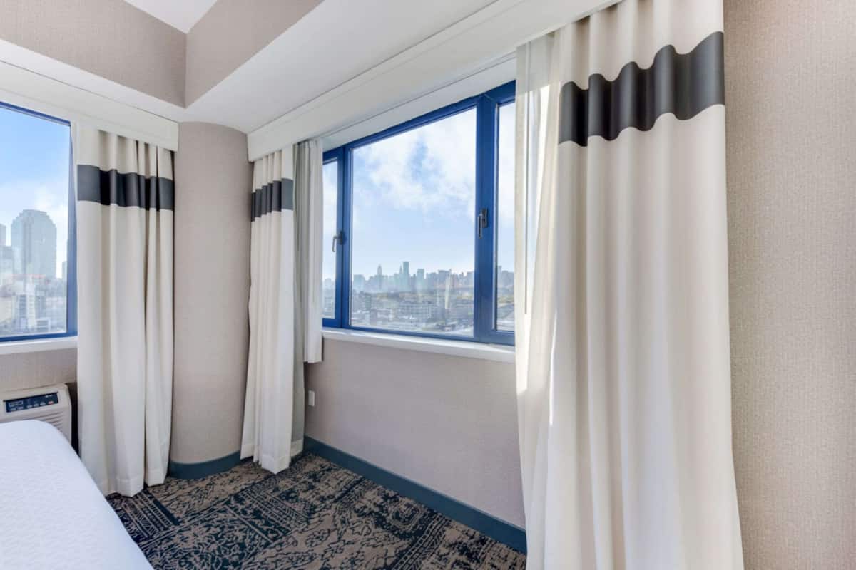 A hotel room with a large window, a bed, and a patterned rug.