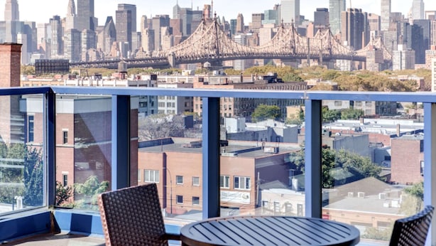 Vista de la ciudad desde un balcón con una mesa y sillas, con vistas a un puente y rascacielos.