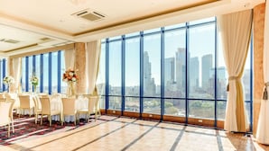 Amplia habitación con un ventanal que ofrece vistas a la ciudad, una mesa larga dispuesta para comer y decoración elegante.