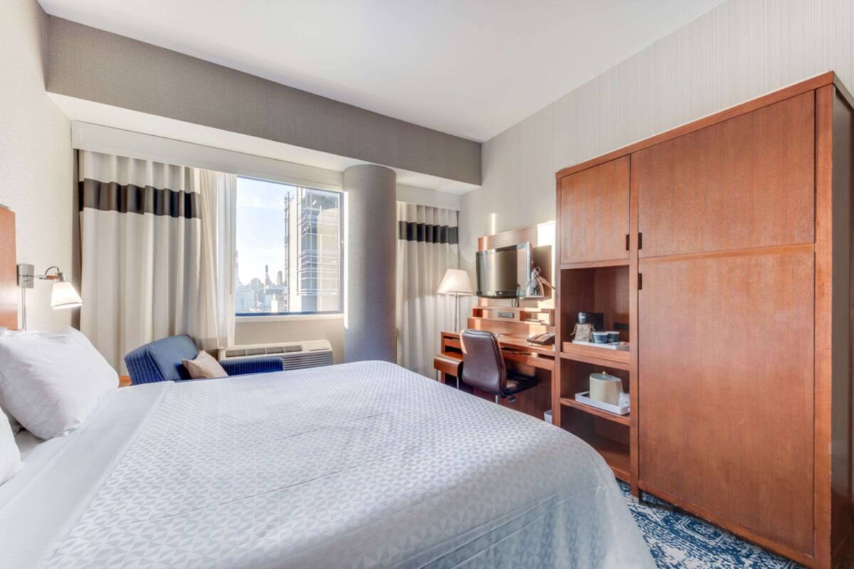 A hotel room with a large bed, a desk, a wardrobe, and a window with curtains.