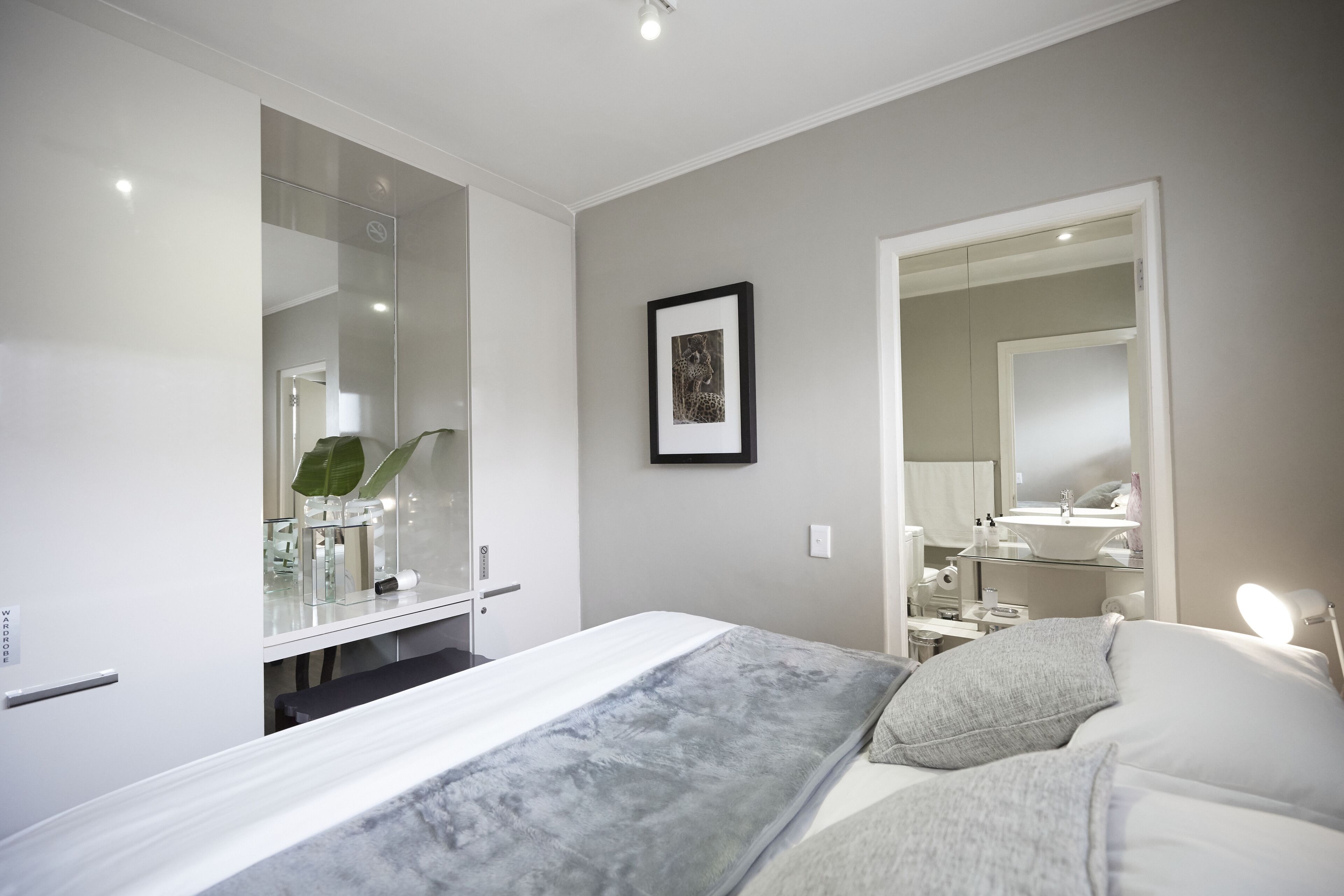 Une chambre à coucher moderne avec un lit, des tables de chevet, un miroir et un tableau encadré au mur.