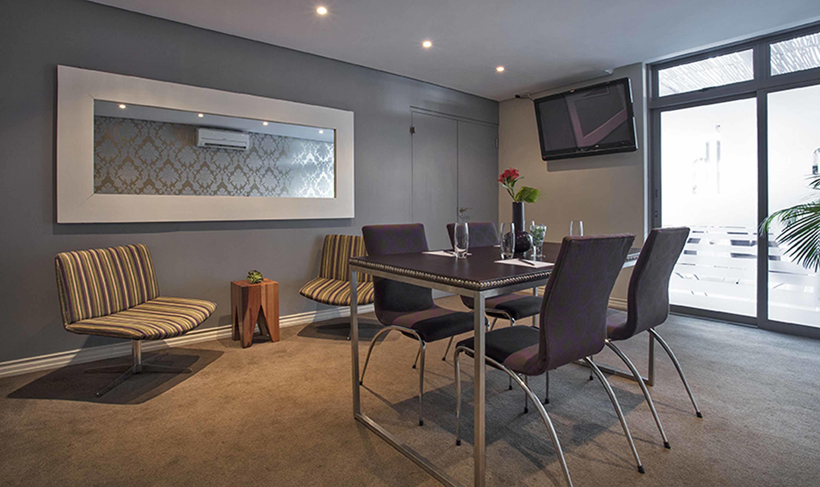 Een moderne vergaderruimte met een glazen tafel, comfortabele stoelen, een klein bijzettafeltje en een groot raam met uitzicht.