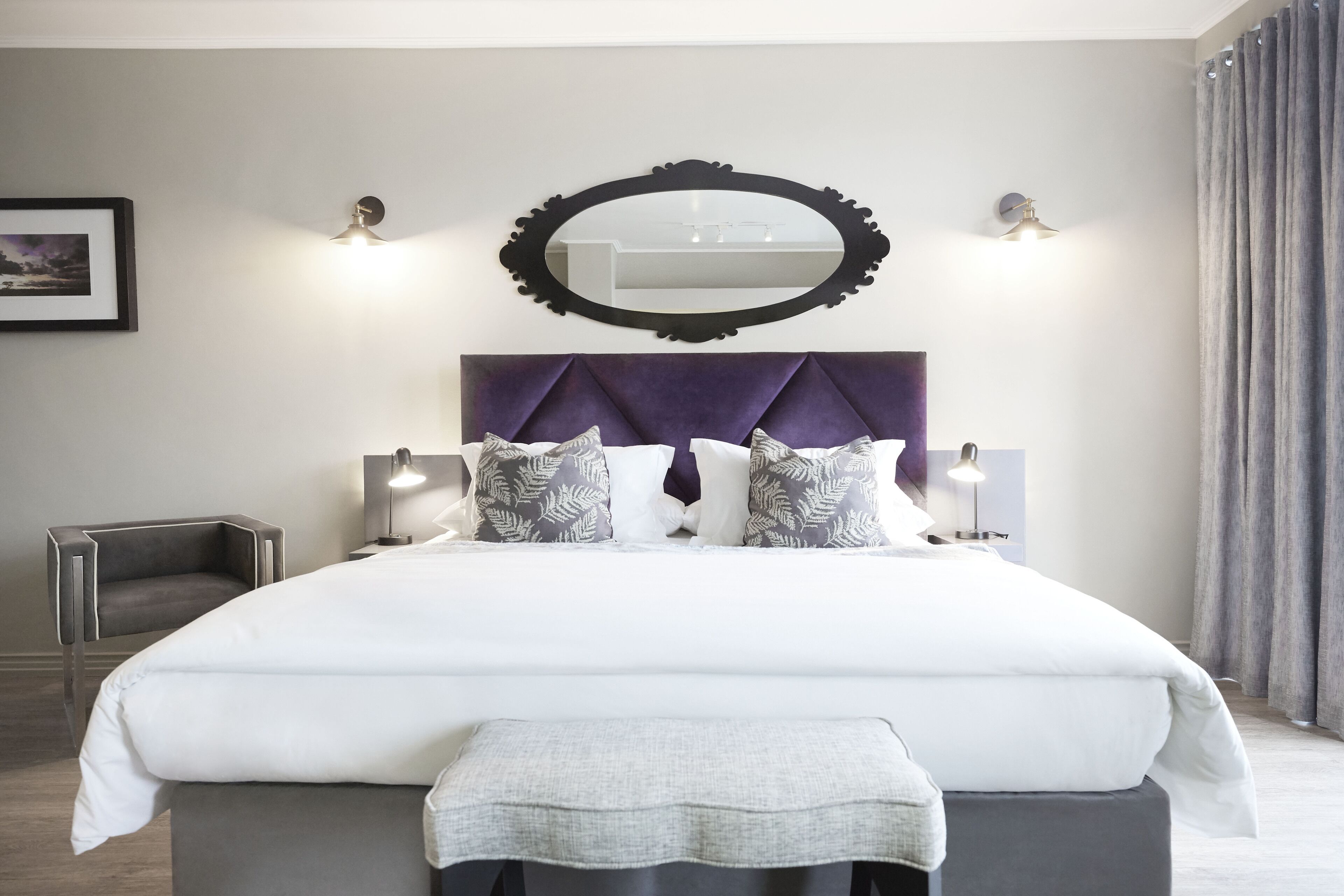 Ein modernes Schlafzimmer mit einem großen Bett, einem Kopfteil, Nachttischlampen, einem Spiegel und einem Sessel.