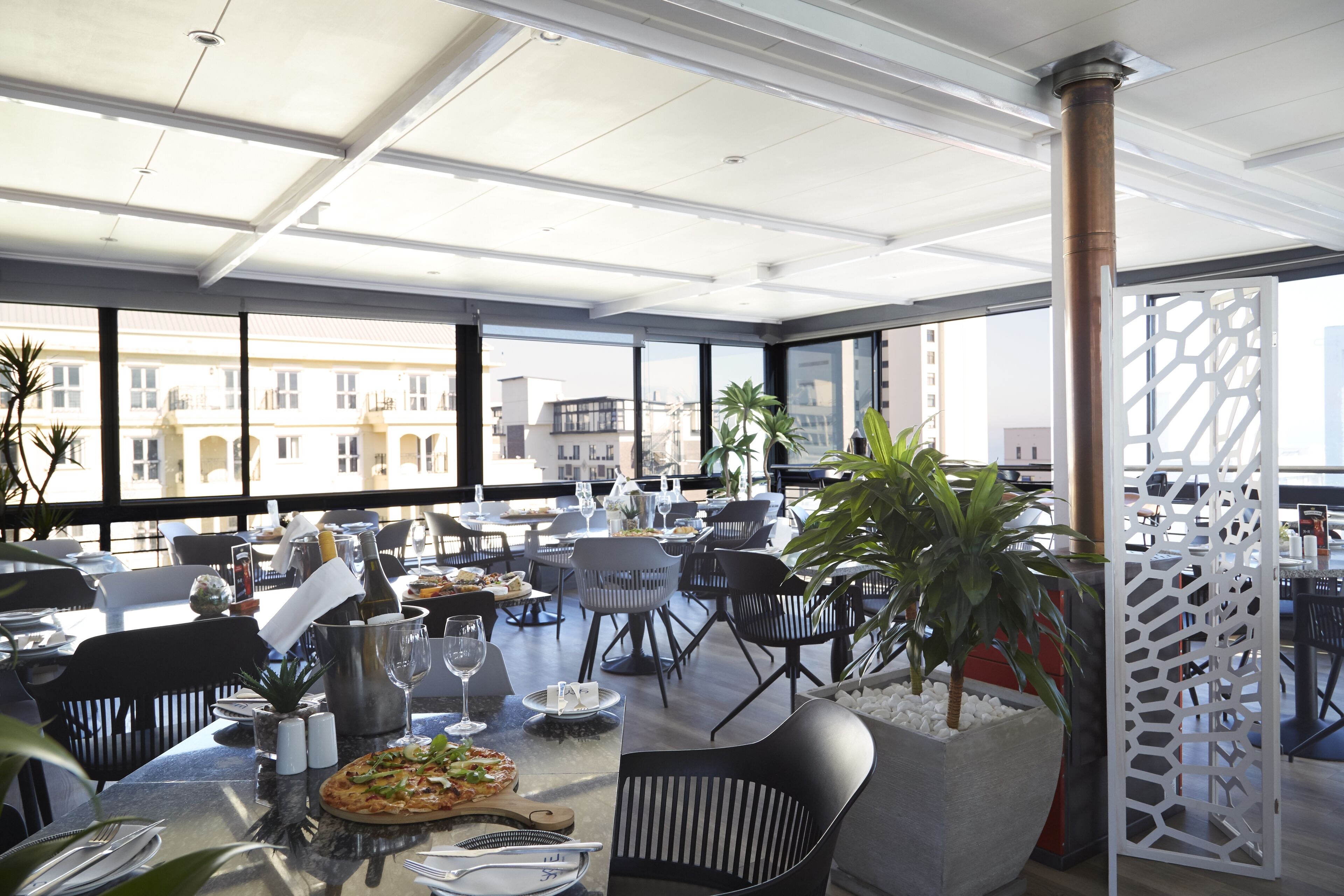 Un espace de restauration moderne, doté de tables, de chaises et d’une grande fenêtre offrant une vue sur la ville.