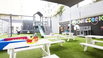 Children can play and explore on the outdoor play structures, slide, and pool, while parents sit at nearby picnic tables.
