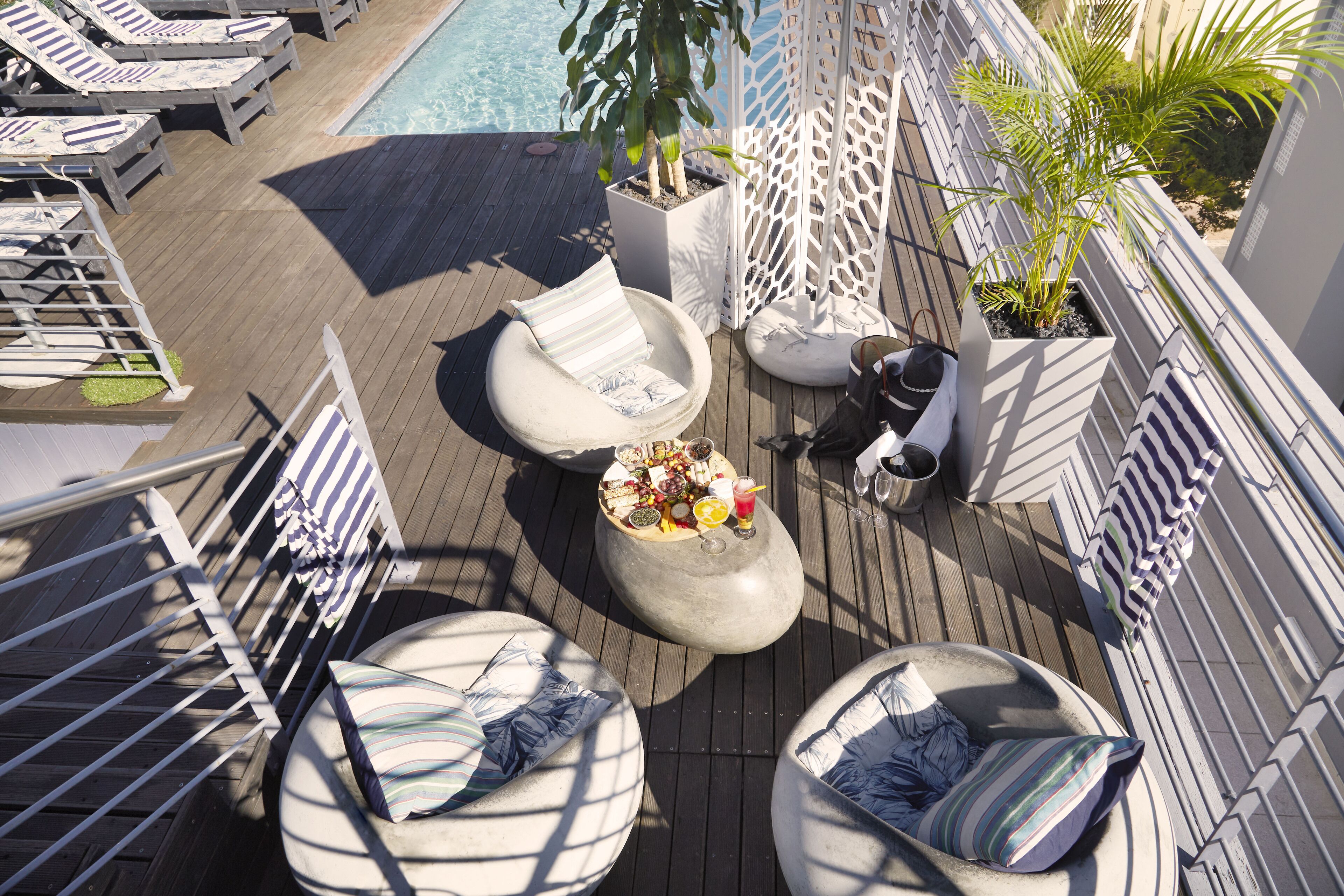 A rooftop deck with lounge chairs, a small table with drinks, and potted plants.