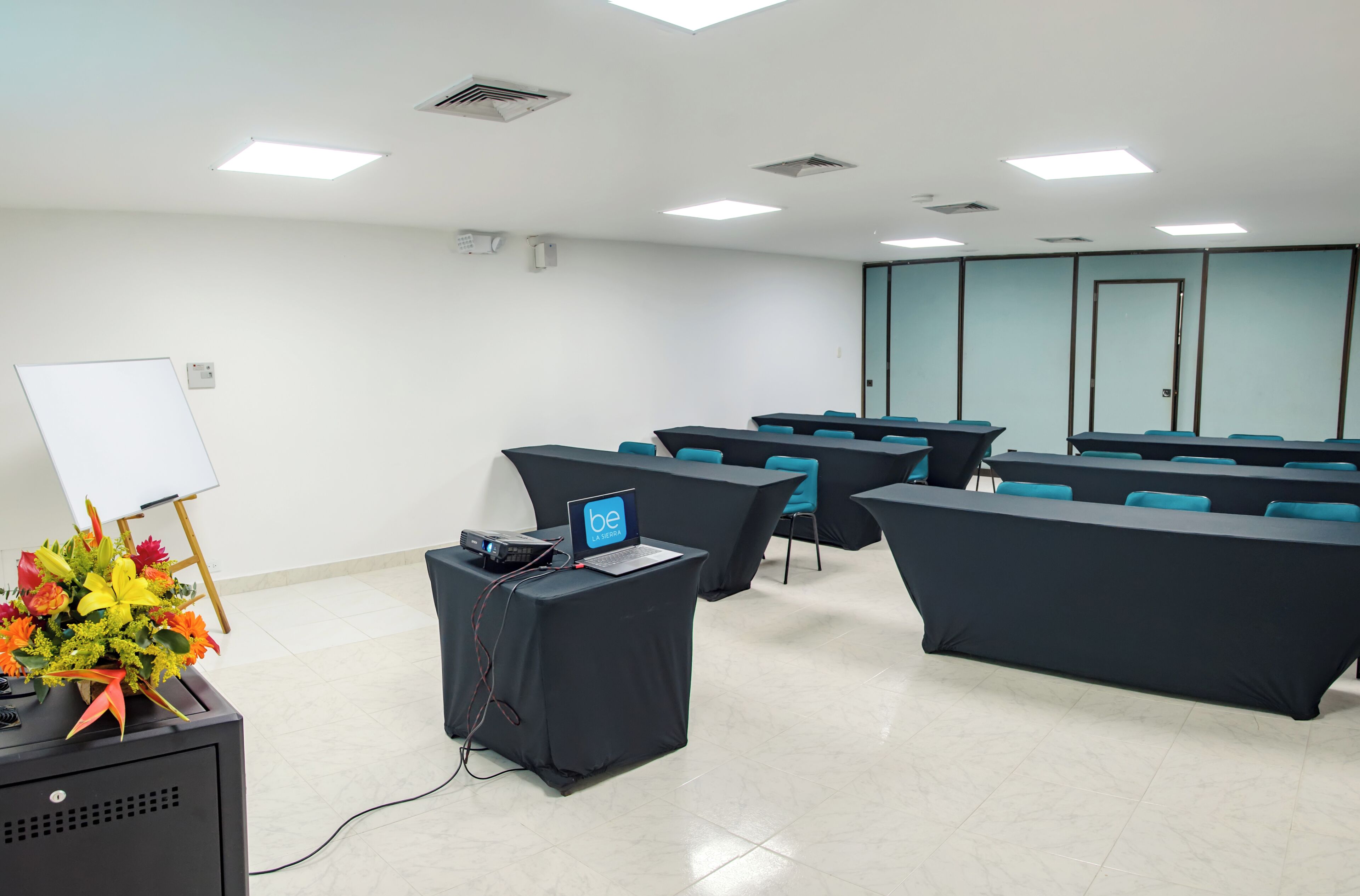 A conference room with multiple tables, a whiteboard, and a laptop on a table.