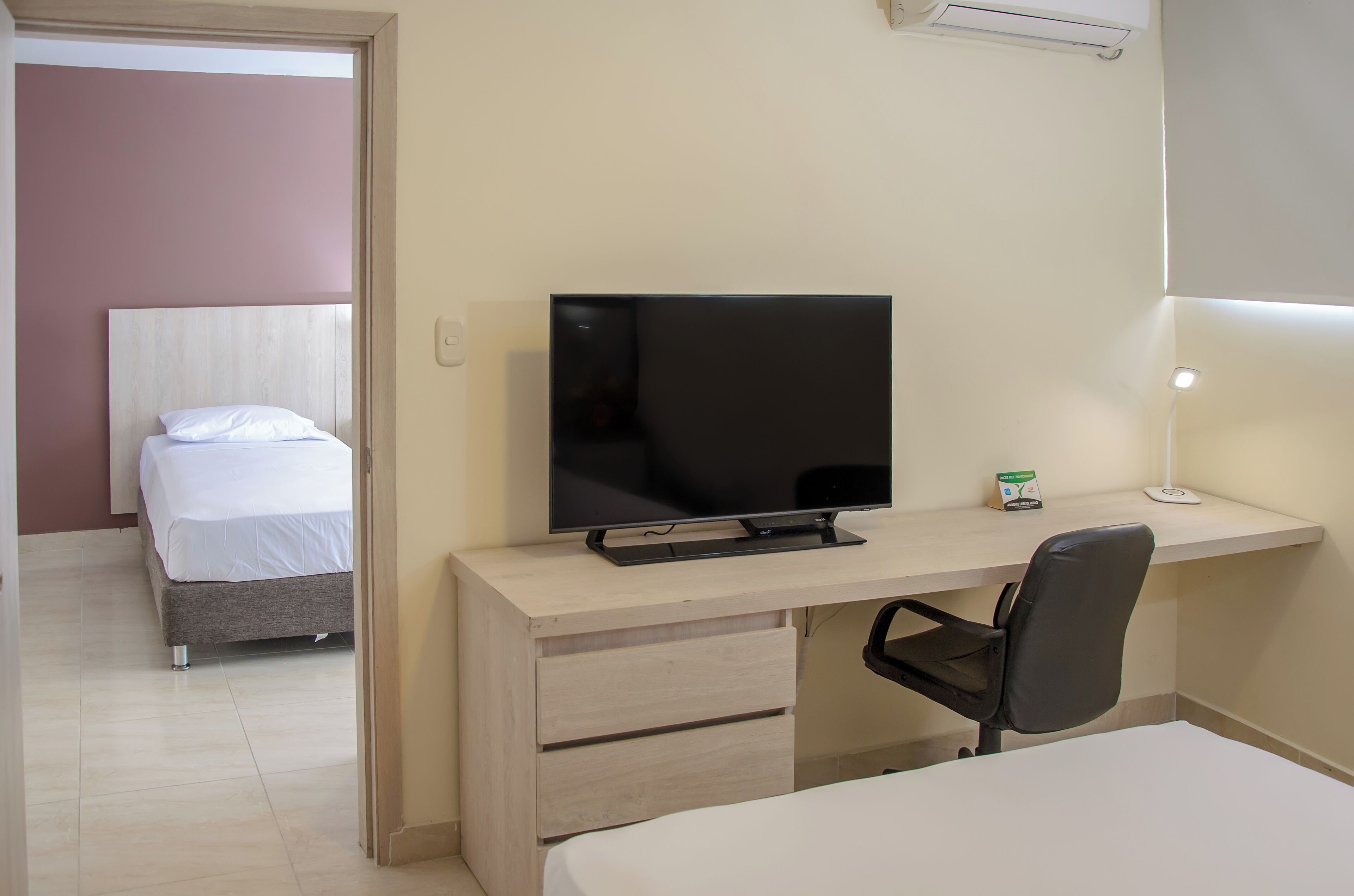 Una habitación de hotel con una cama, un escritorio con televisor, una silla y una mesita de noche.