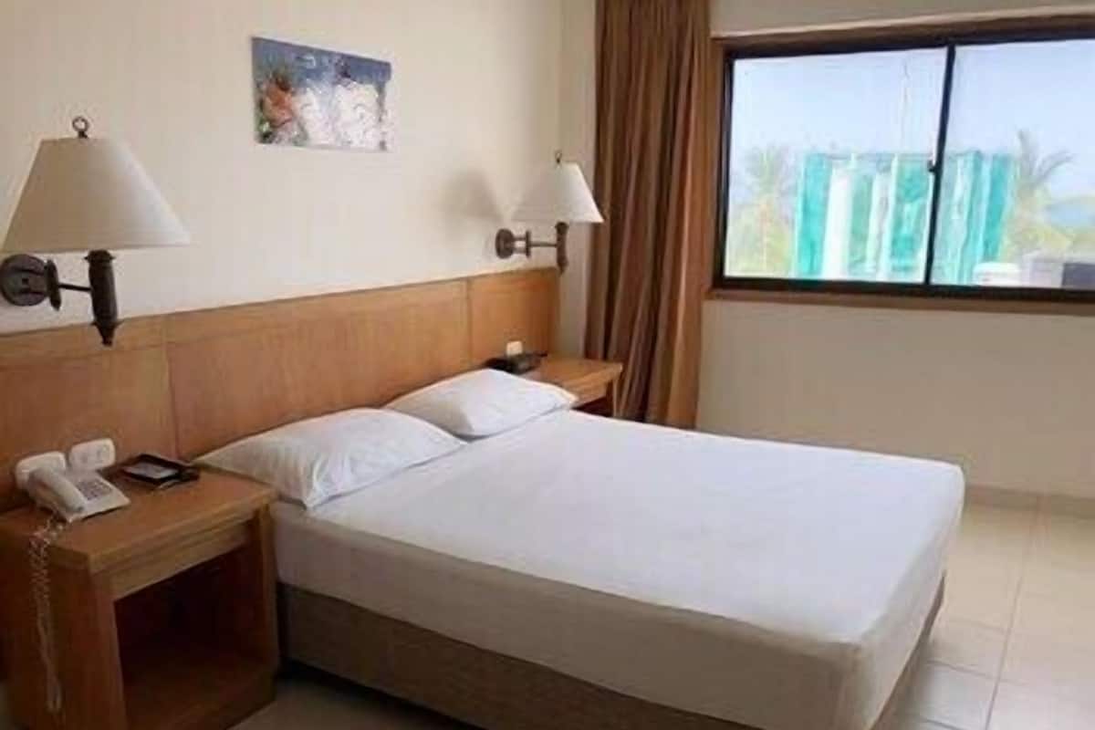 Une chambre d’hôtel avec un lit, deux tables de chevet, un téléphone et une fenêtre avec des rideaux.