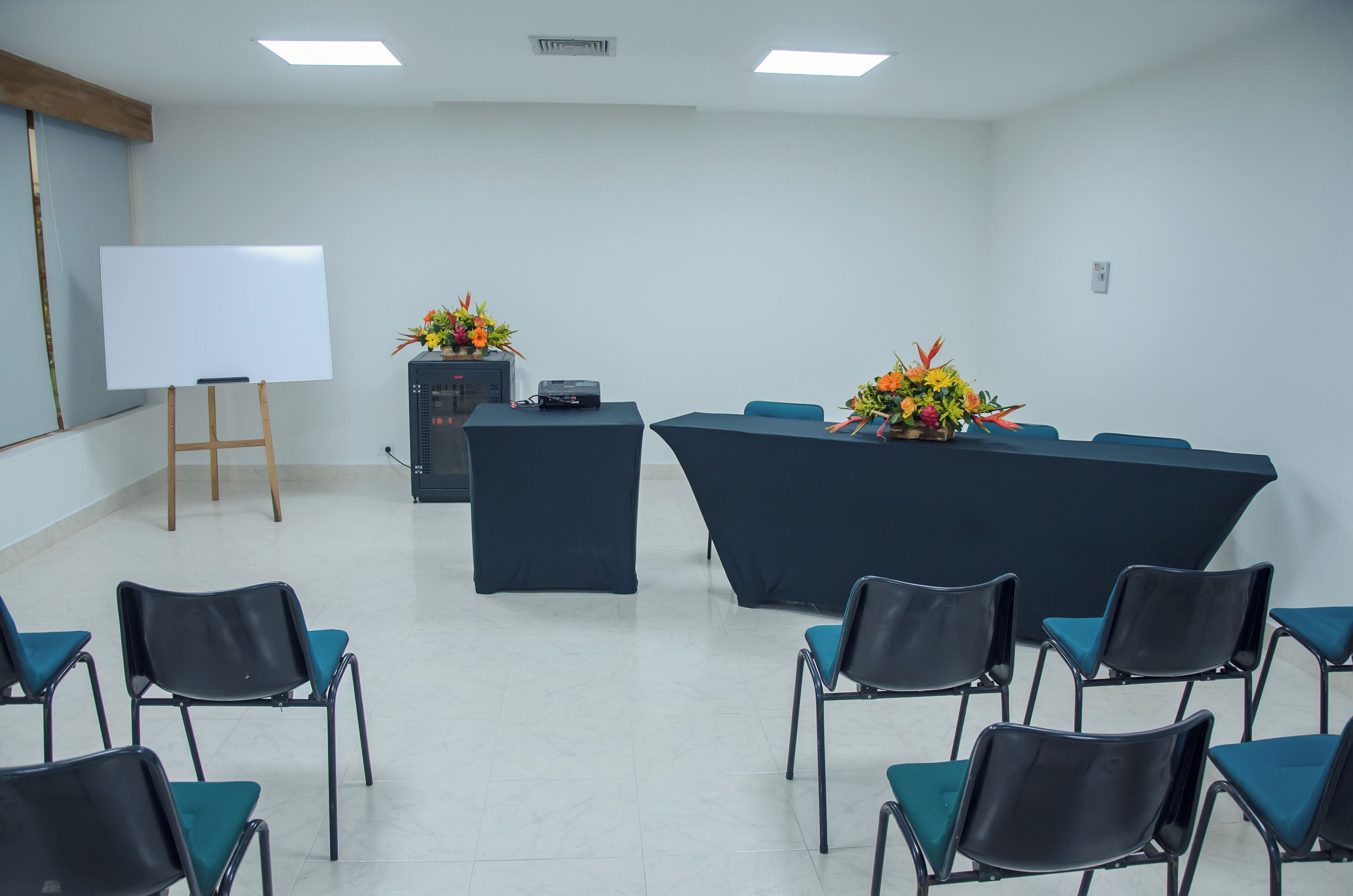 Una sala de conferències amb pissarra, projector i centrals florals damunt d'una taula.
