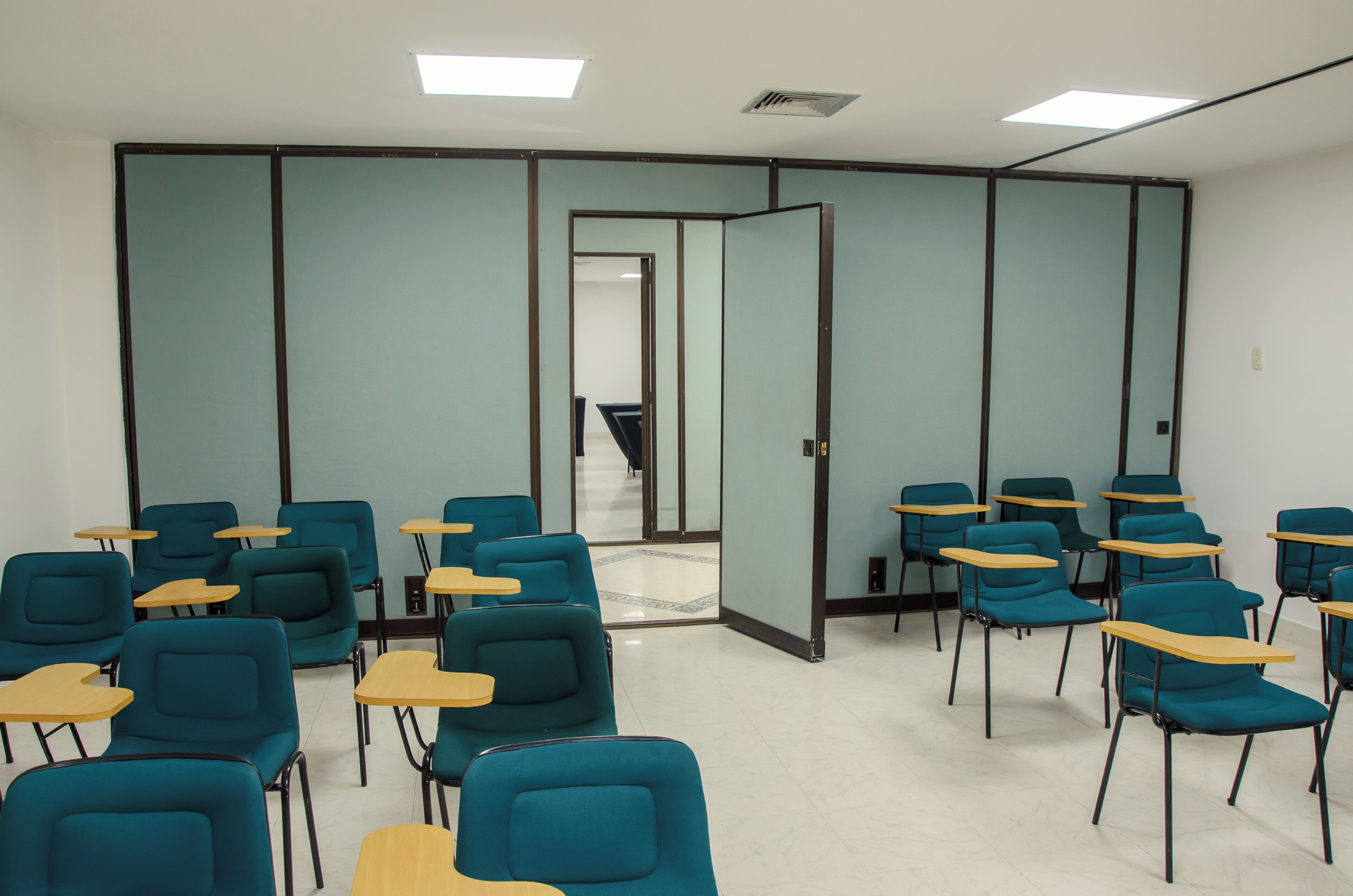 A classroom with teal chairs and wooden desks arranged in rows.