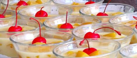 Multiple clear glass cups filled with a creamy dessert, topped with a red cherry and pieces of fruit.