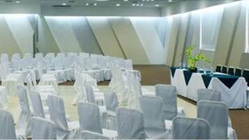 A conference room with rows of white-covered chairs and tables, arranged in a semi-circle.
