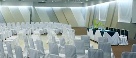 Une salle de conférence avec des rangées de chaises et de tables recouvertes de tissu blanc, disposées en demi-cercle.