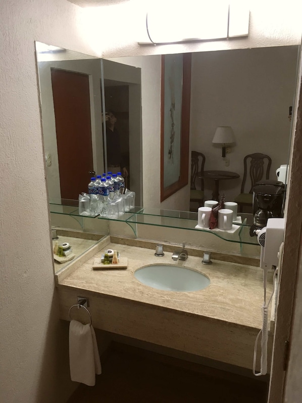 A bathroom with a glass-topped sink, a mirror, and a towel rack.