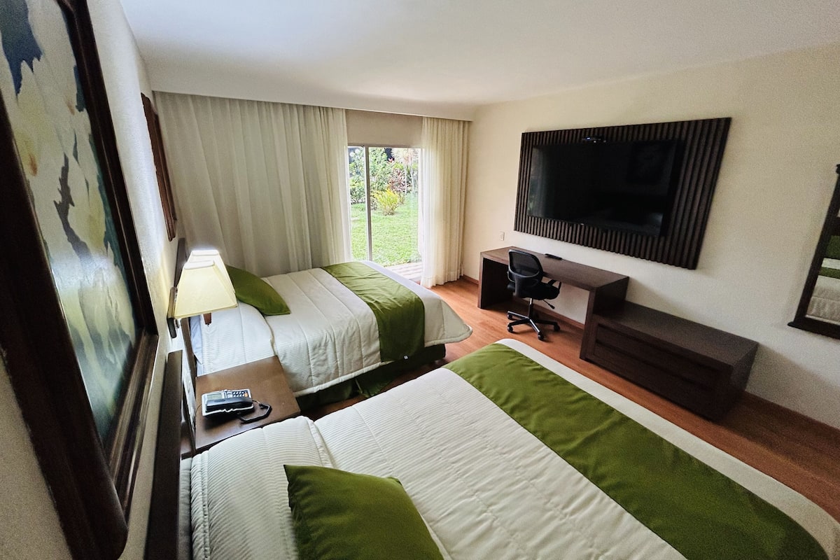 Ein Hotelzimmer mit zwei Betten, einem Schreibtisch, einem Stuhl, einem Fernseher und einem Fenster mit Vorhängen.