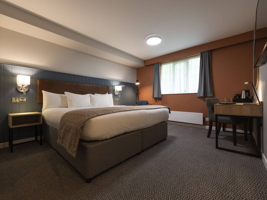 A hotel room with a large bed, bedside tables, a desk, and a chair.