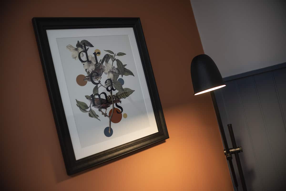 A framed artwork on a wall, a black floor lamp, and a door with a metallic handle.