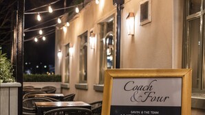 An outdoor seating area with tables and chairs, string lights, and a welcome sign for Coach & Four.