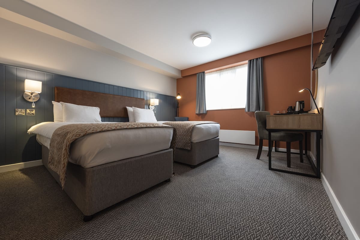 A hotel room with two beds, a desk, and a chair.
