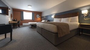 A hotel room with a large bed, a desk, a chair, and a window with curtains.