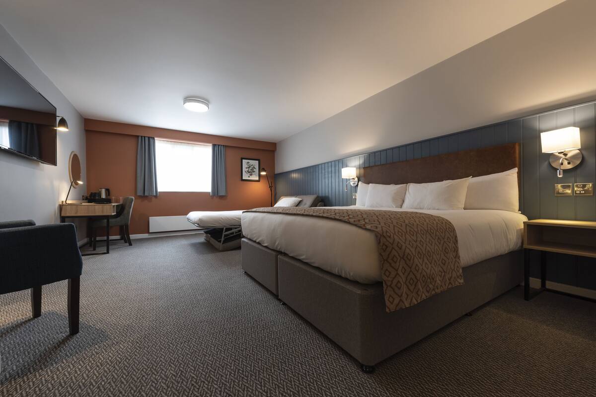 A hotel room with a large bed, a desk, a chair, and a window with curtains.