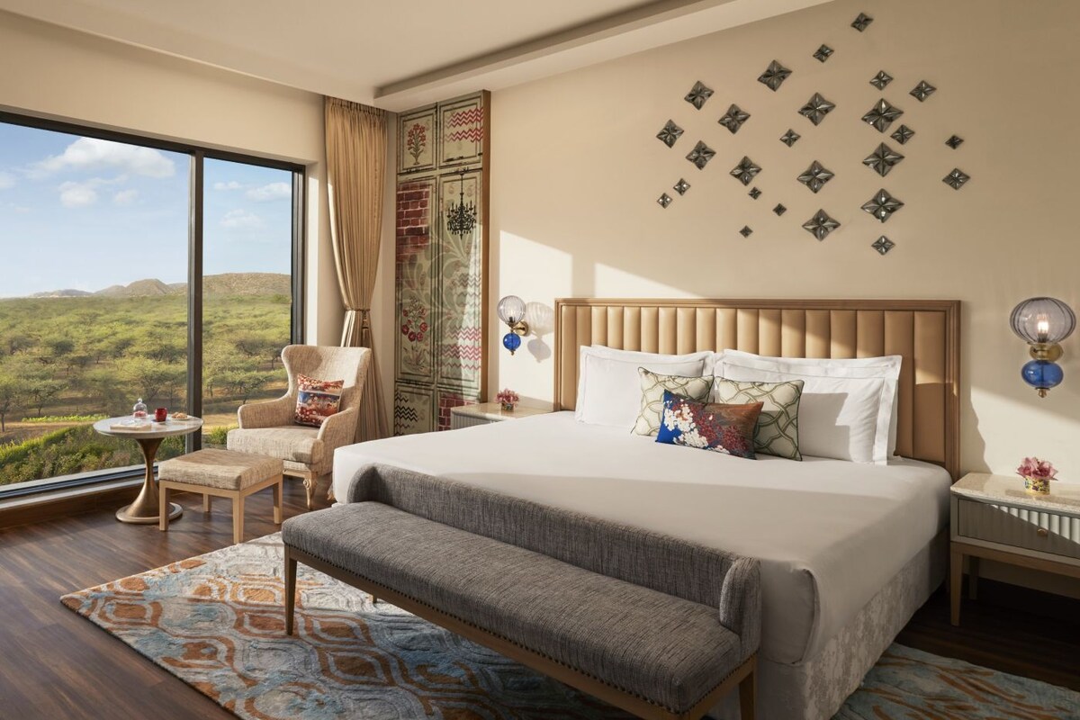Un dormitorio con una cama grande, una silla, una mesita y vistas al exterior, además de decoración en las paredes.