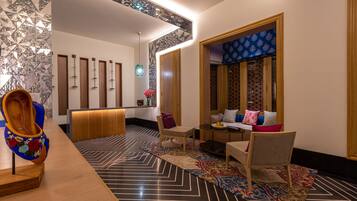 Een moderne hotellobby met een receptiebalie, zithoek en decoratieve elementen zoals een vaas en kamerbreed tapijt.