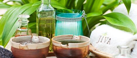 Un ambiente de spa con una bandeja de madera que contiene varios productos de baño, una botella de vidrio verde, un recipiente de vidrio azul y una toalla blanca con la palabra 'JIVA' escrita.