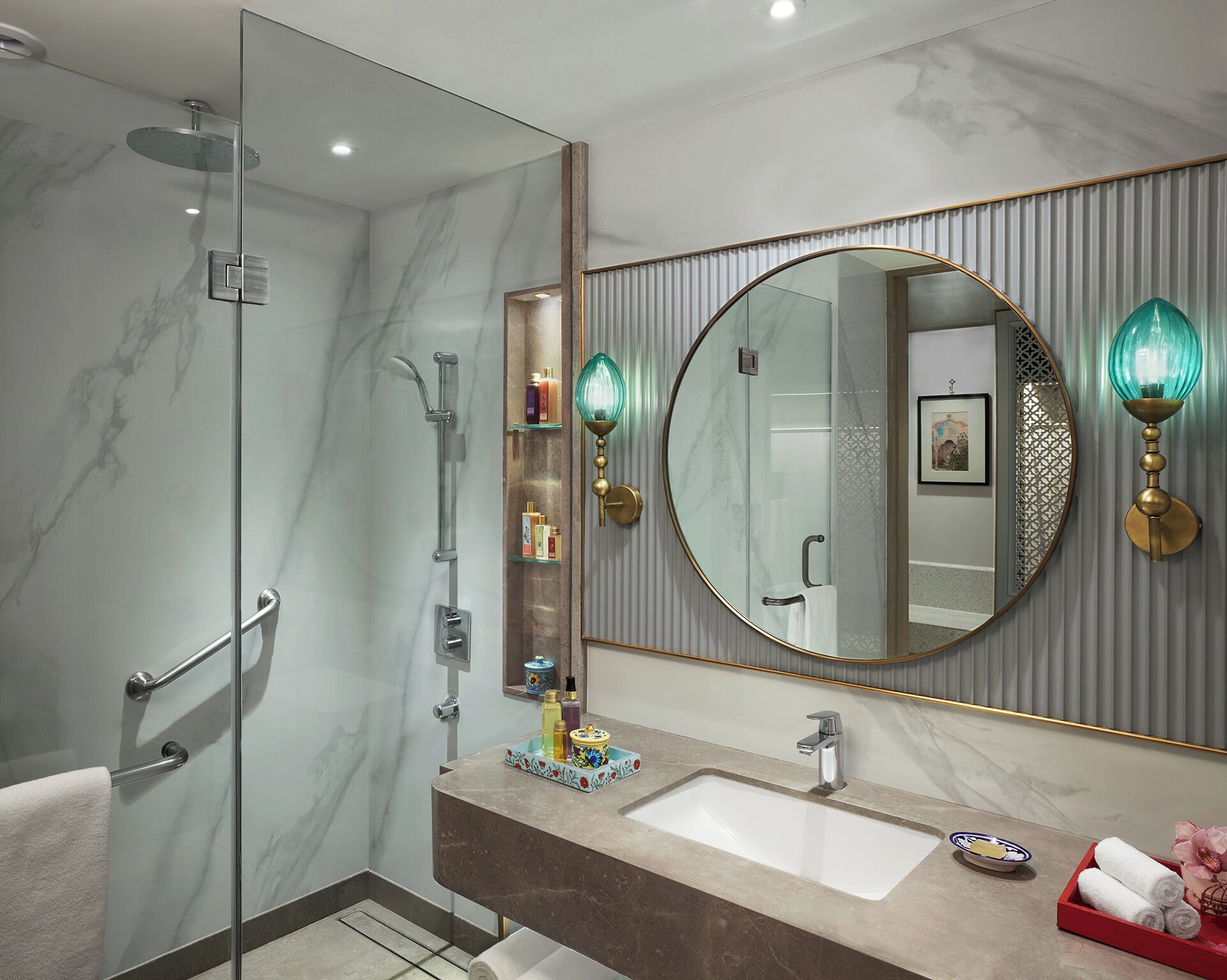 A modern bathroom with a glass-enclosed shower, a marble vanity, a large mirror, and wall-mounted sconces.
