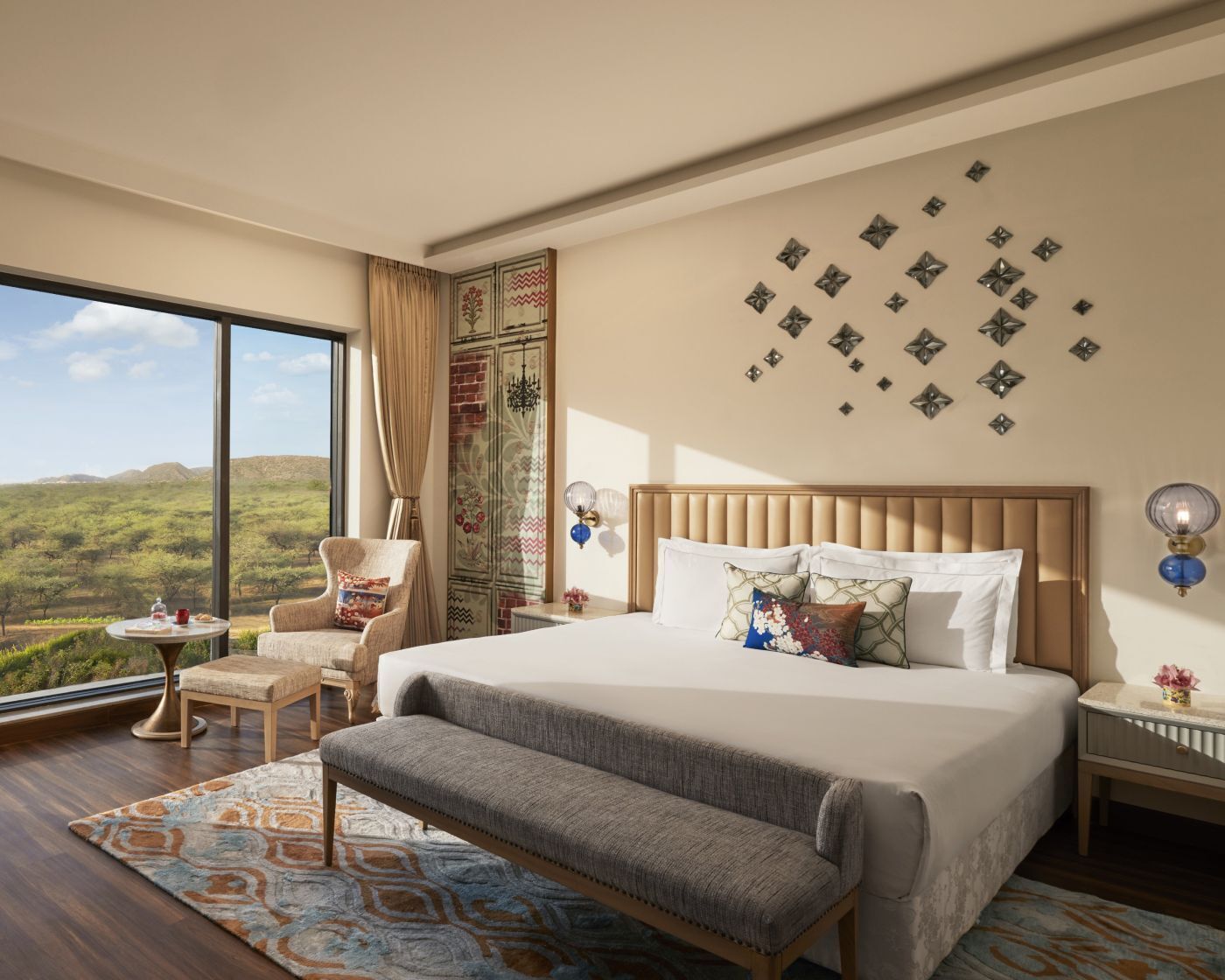 A bedroom with a large bed, a chair, a small table, a view of the outdoors, and decorative wall art.